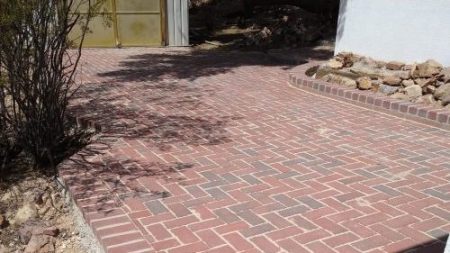 An outdoor patio area constructed from red brick flagstone pavers in a basketweave pattern, surrounded by natural desert landscaping.