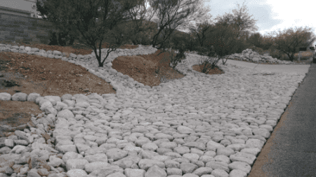A desert yard with a pathway bordered by large, natural rip rap rocks for erosion control and a decorative effect.