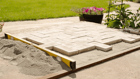 Close-up of a new patio being installed with light-colored paving stones laid out on a base of sand.